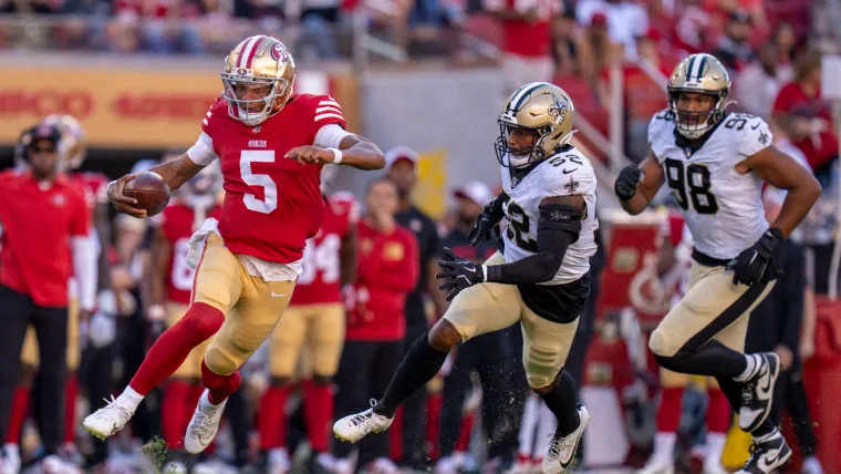 August 18, 2024; Santa Clara, California, USA; San Francisco 49ers quarterback Joshua Dobbs (5) runs the football against New Orleans Saints linebacker D'Marco Jackson (52) and defensive end Payton Turner (98) during the second quarter at Levi's Stadium. Mandatory Credit: Kyle Terada-USA TODAY Sports